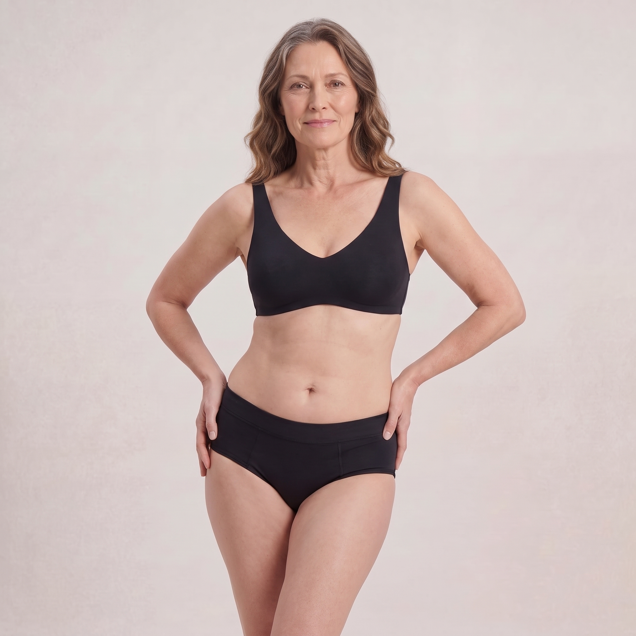 A woman modeling a matching black bra and underwear set against a plain, light beige studio background.
